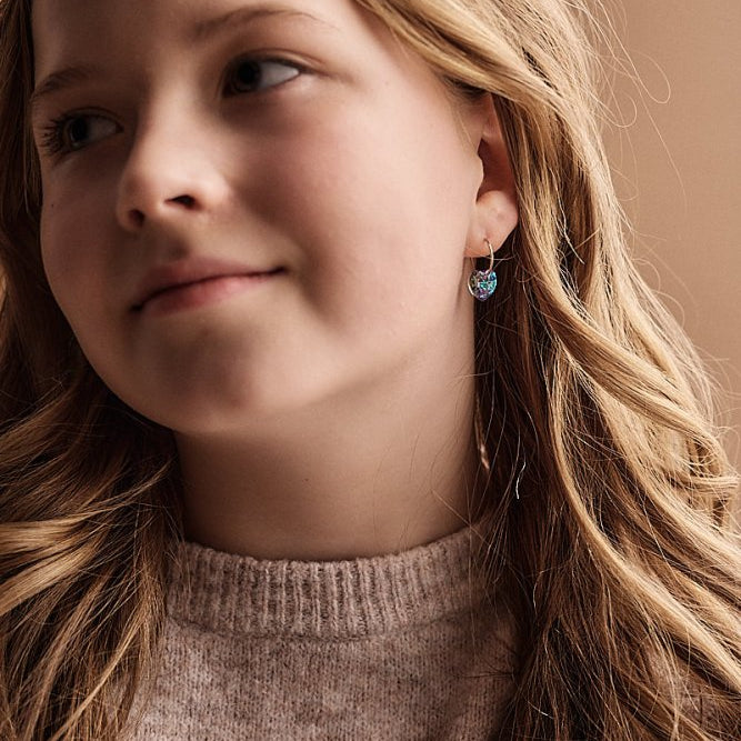 tienermeisje met een setje titanium oorringen van Blomdahl in Aan de oorringetjes hangen paarse hartjes.