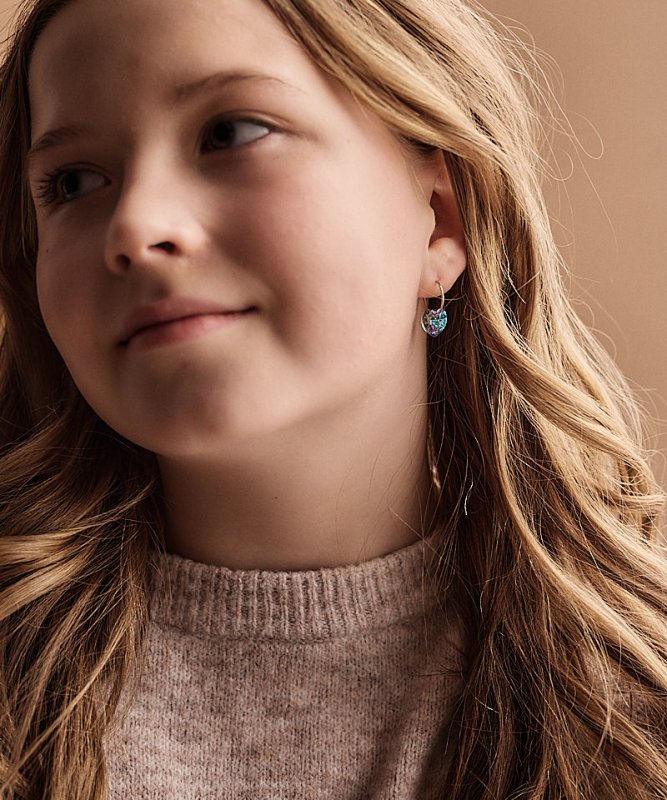 tienermeisje met een setje titanium oorringen van Blomdahl in Aan de oorringetjes hangen paarse hartjes.